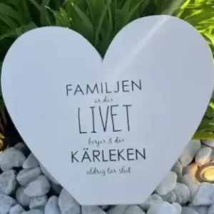 a white heart shaped sign in front of green plants